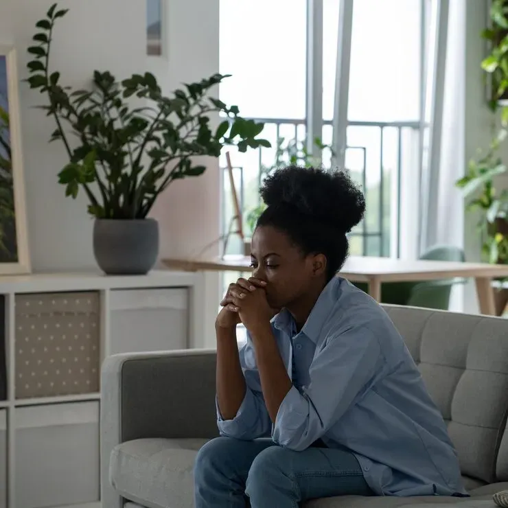 Woman sitting on a sofa feeling anxious and overwhelmed, considering mental health support in Katy, TX